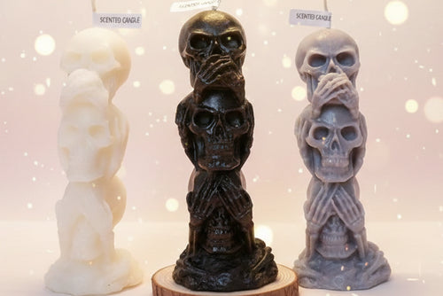 Three skull-shaped candles with labels on a white surface.