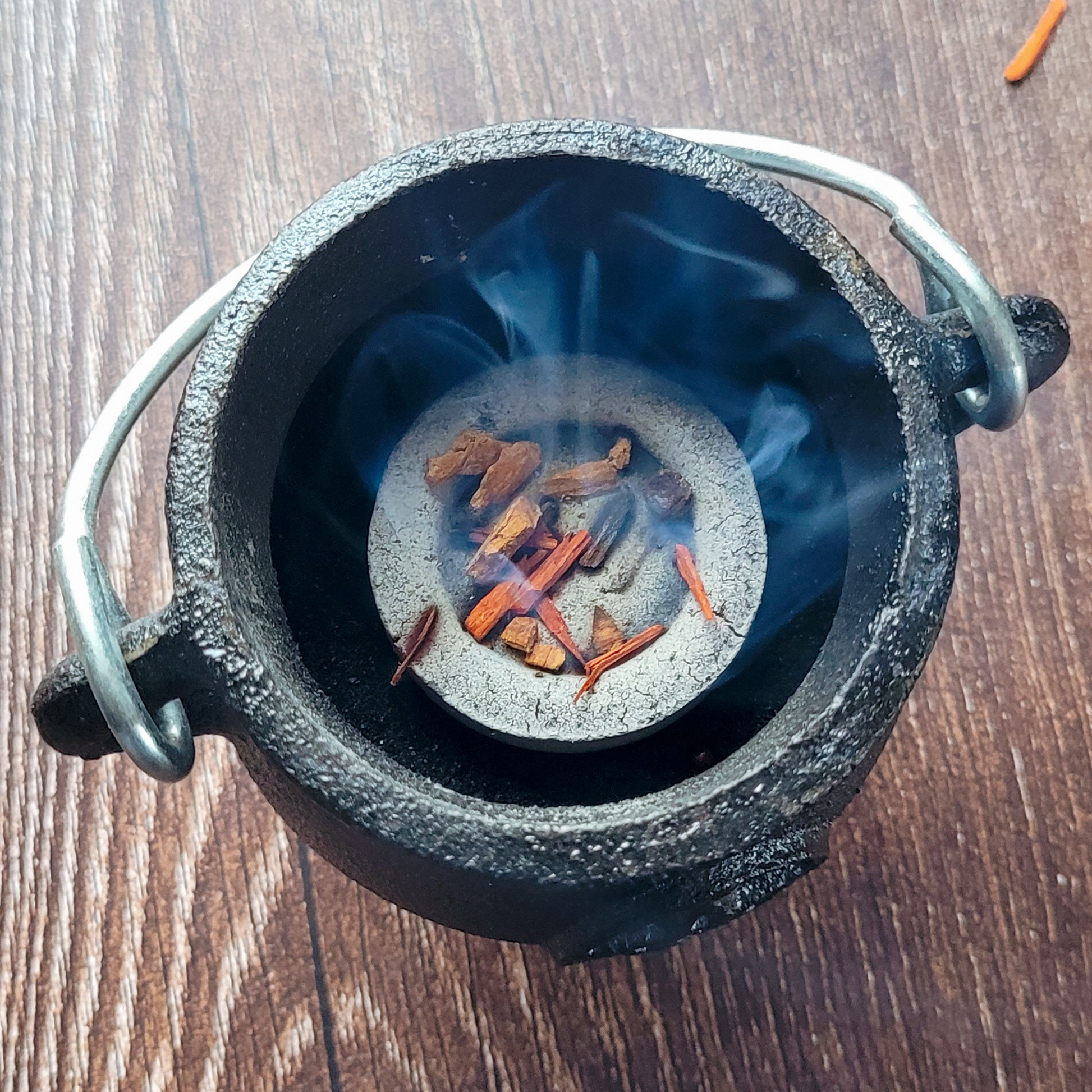 Black cauldron with burning incense sticks on a wooden surface