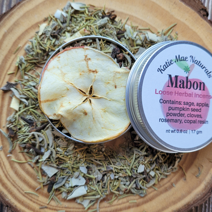 Herbal incense with an apple slice and 'Katie Mae Naturals Mabon' packaging on a wooden surface.