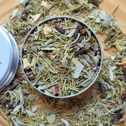 Metallic container filled with a mix of dried herbs and spices on a wooden surface.