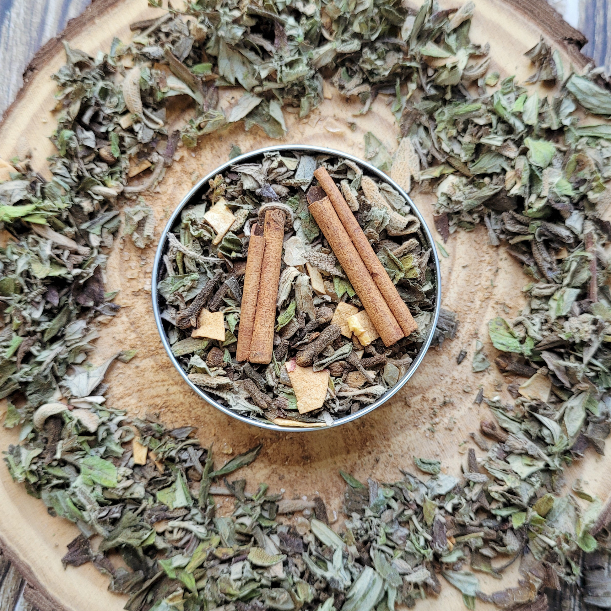 Dried herbs and cinnamon sticks in a metal container on a wooden surface