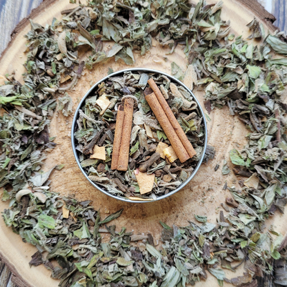 Dried herbs and cinnamon sticks in a metal container on a wooden surface