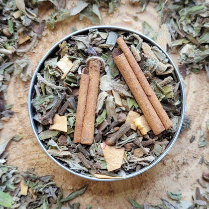 Metal bowl filled with dried herbs and cinnamon sticks on a wooden surface