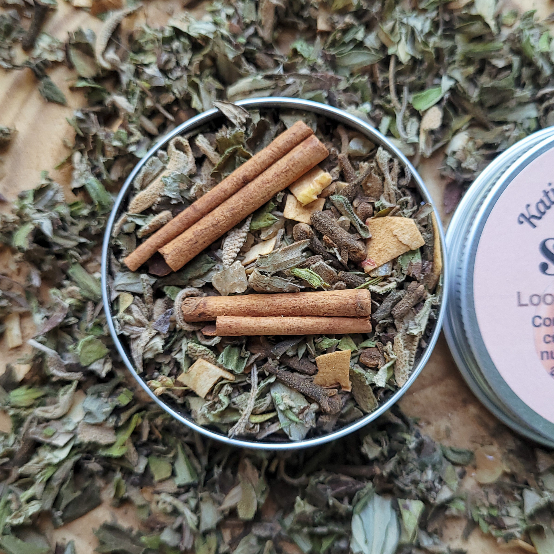Herbal mix with cinnamon sticks in a metal container on a wooden surface
