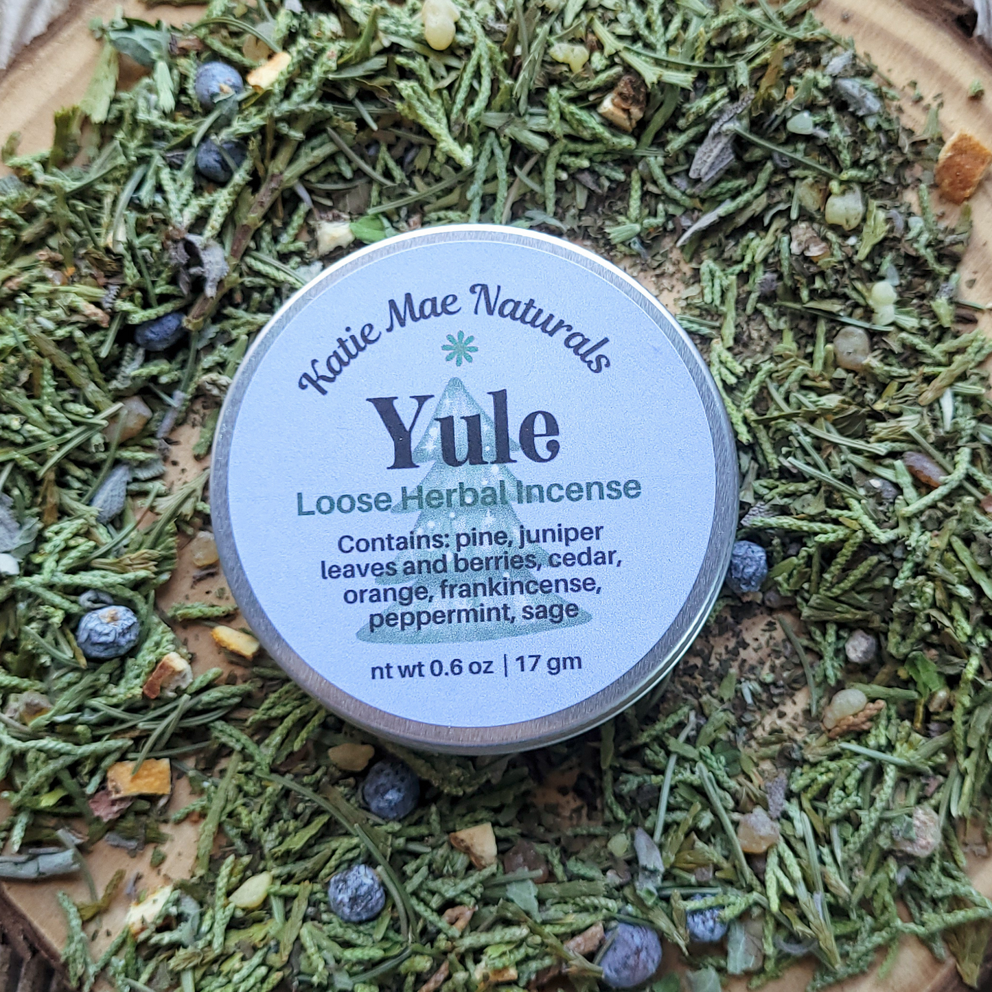 Katie Mae Naturals Yule Loose Herbal Incense container on a bed of green herbs and berries
