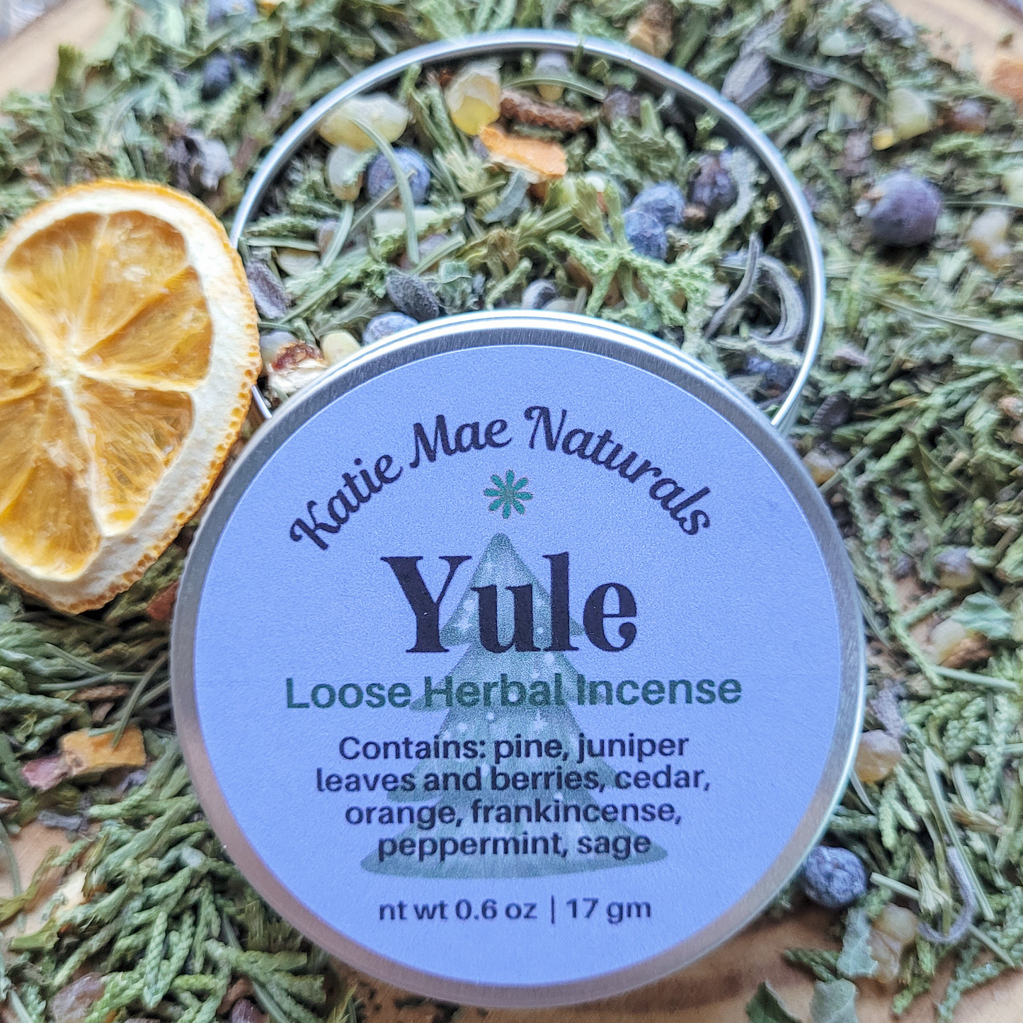 Katie Mae Naturals Yule loose herbal incense packaging on a bed of dried herbs and spices.