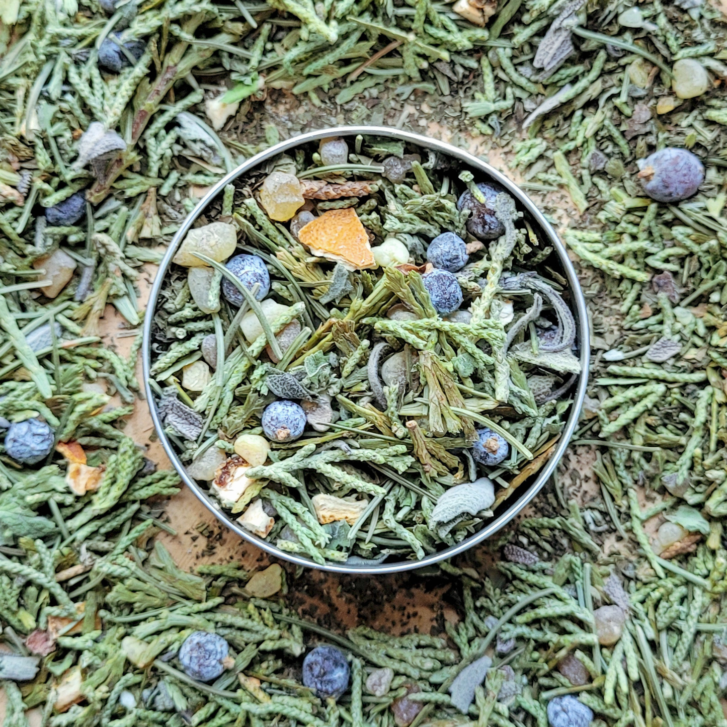 Metallic container filled with a mix of dried herbs and berries on a textured green background
