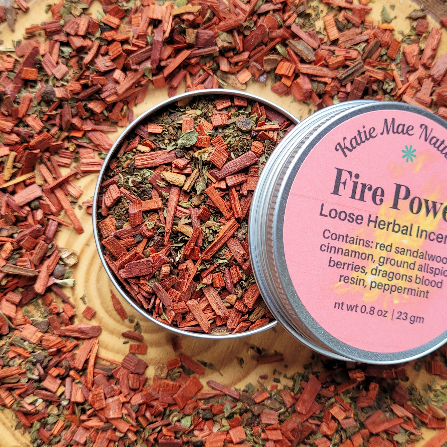 Loose herbal incense in a tin with a pink label on a wooden surface.