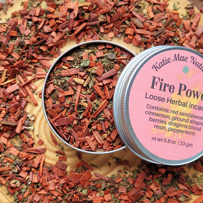 Loose herbal incense in a tin with a pink label on a wooden surface.