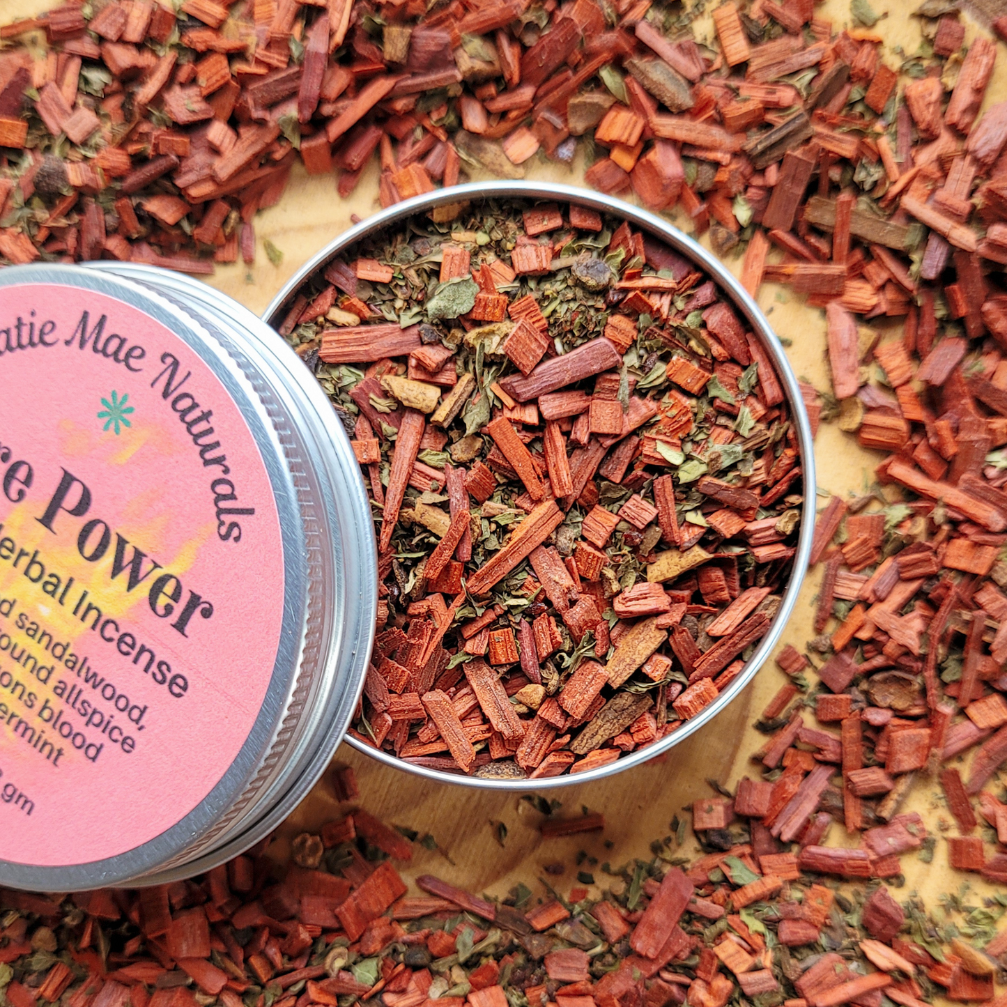 Herbal incense in a metal container with a pink label on a wooden surface.