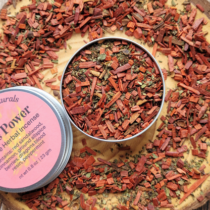 Herbal incense sticks in a metal tin surrounded by loose incense on a wooden surface.