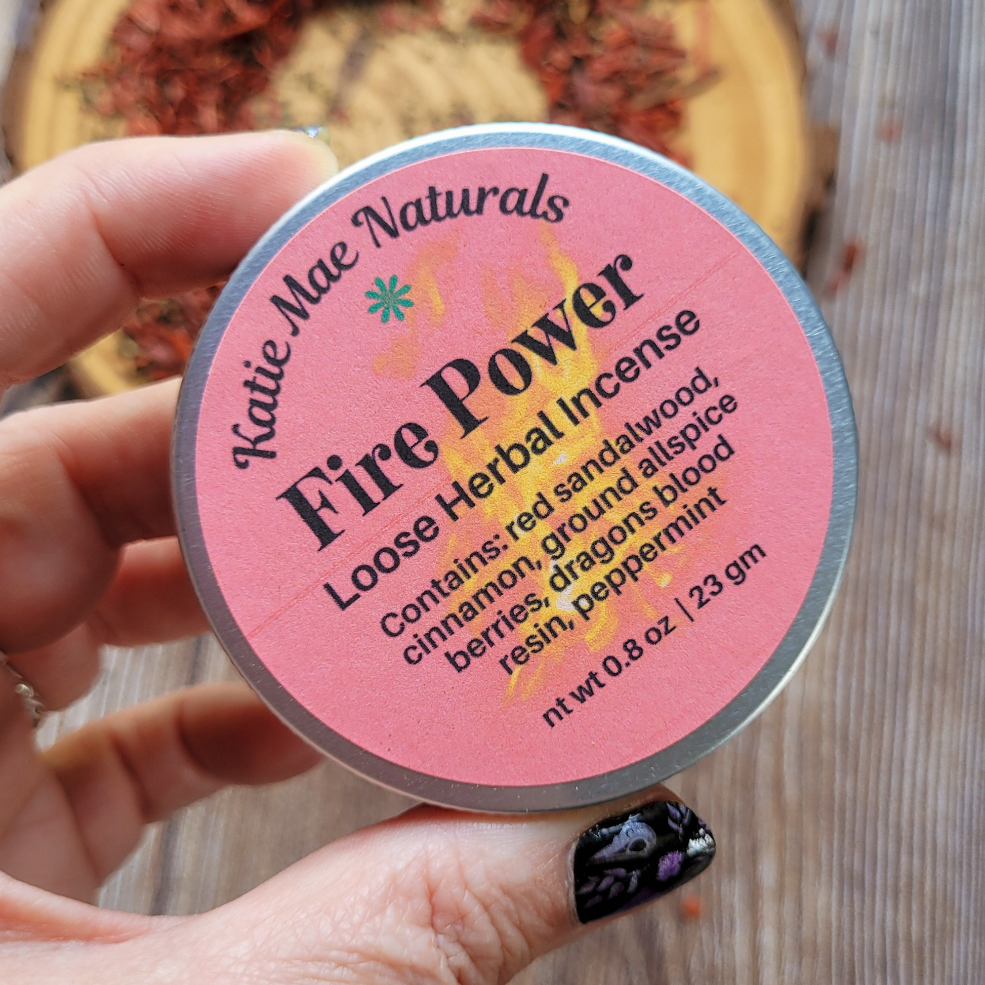 Katie Mae Naturals Fire Power loose herbal incense container held by a hand with black nail polish.