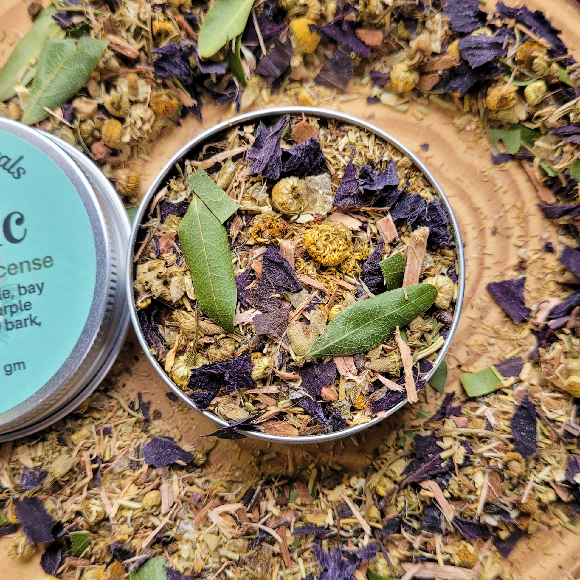 Metal tin filled with dried herbs and leaves on a bed of similar herbs.