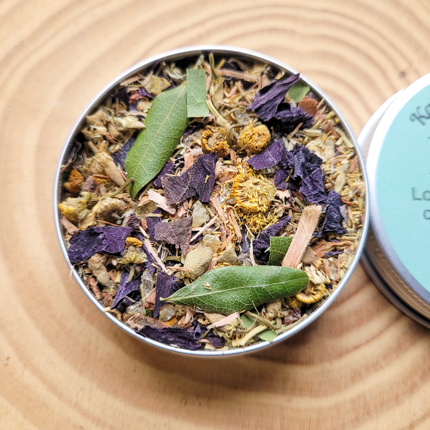 Metal tin filled with dried herbs and flowers on a wooden surface