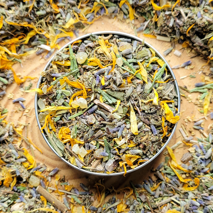 Metallic bowl filled with dried herbs and flowers on a wooden surface.
