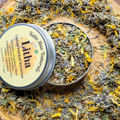 Herbal incense in a tin with 'Katie Mae Naturals' branding, surrounded by dried herbs and flowers.