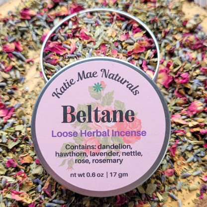 Katie Mae Naturals Beltane Loose Herbal Incense packaging on a bed of dried herbs.