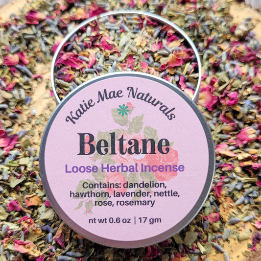 Katie Mae Naturals Beltane Loose Herbal Incense packaging on a bed of dried herbs.