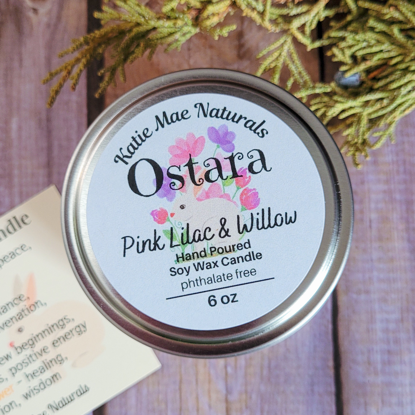 Katie Mae Naturals Ostara Pink Lilac & Willow candle lid on a wooden surface with greenery.