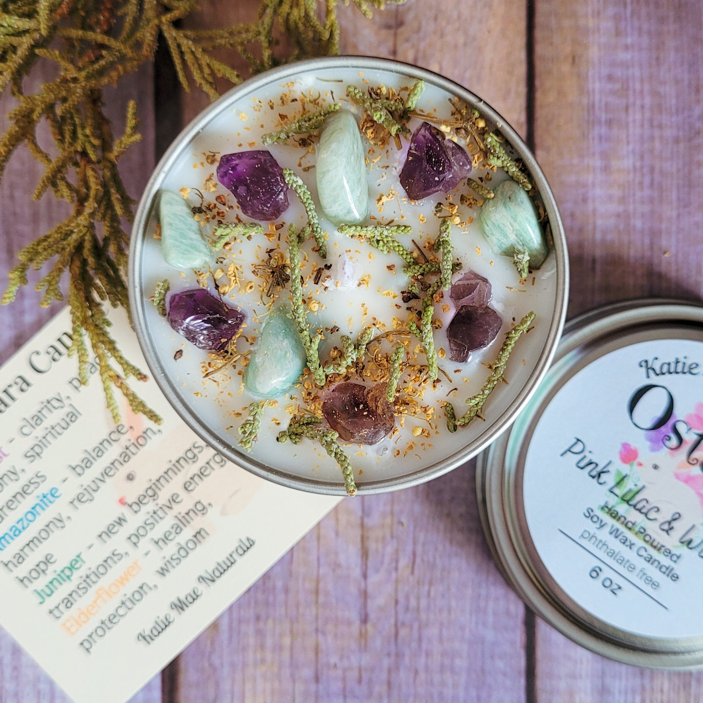 Candle with crystals and herbs on a wooden surface, next to a label with product details.