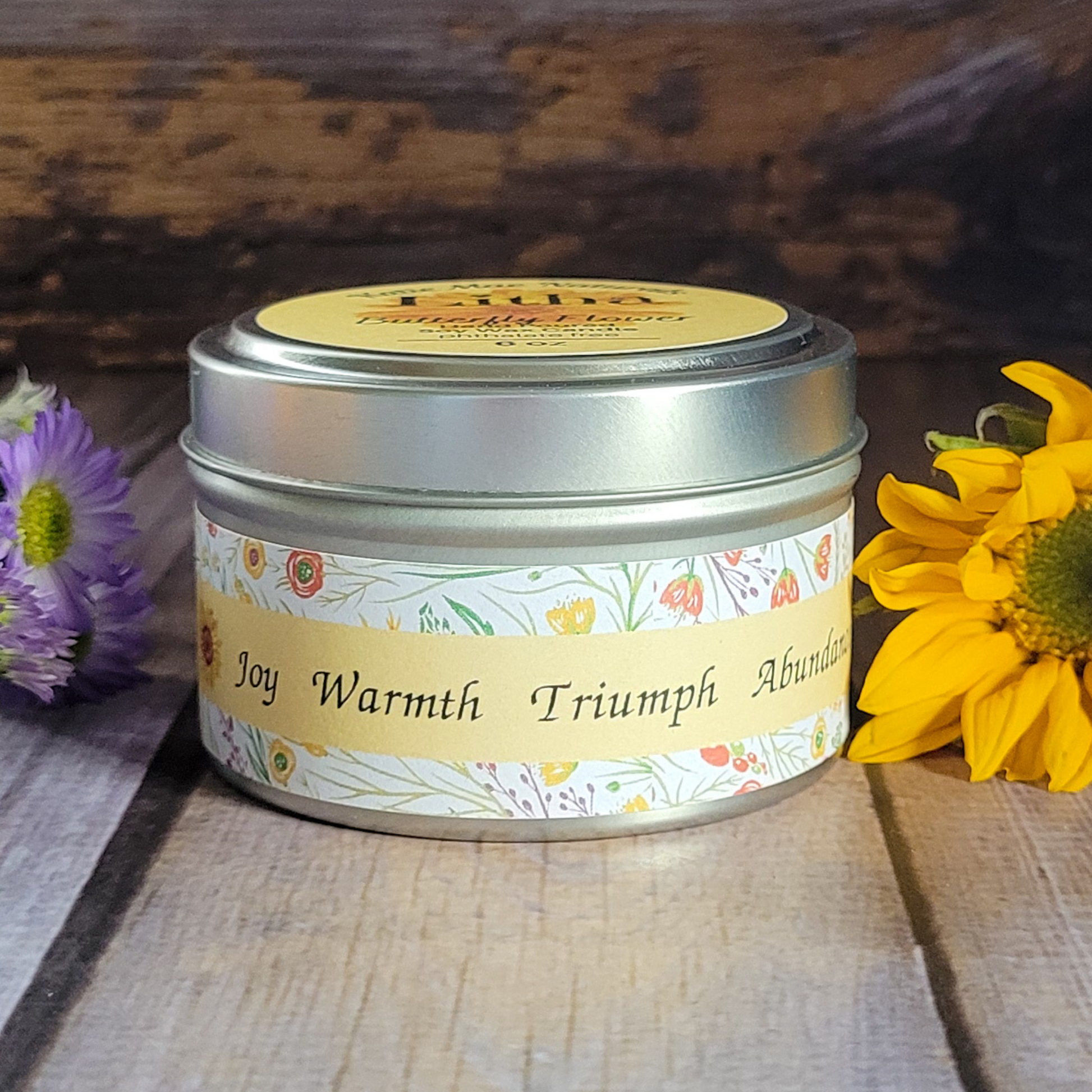 Candle tin with floral design and text on a wooden surface with flowers.