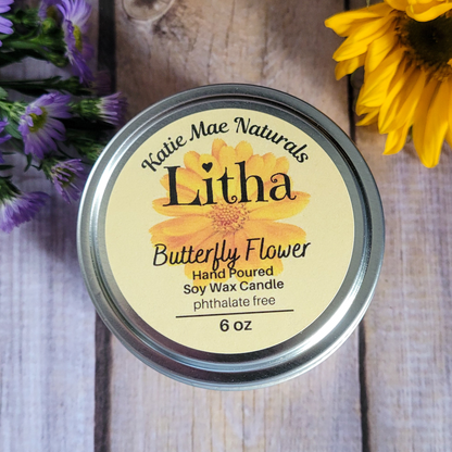 Katie Mae Naturals Litha Butterfly Flower candle on a wooden surface with flowers around