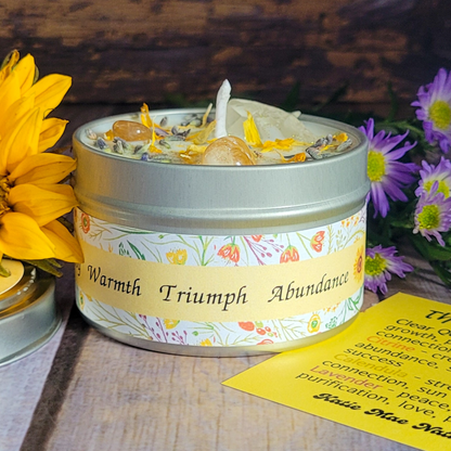 Candle in a tin with decorative label surrounded by flowers on a wooden surface