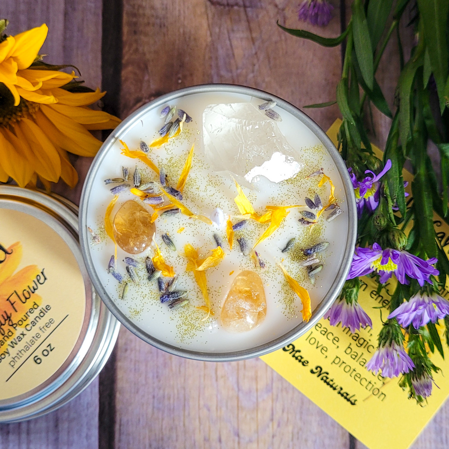 Candle in a tin with floral elements on a wooden surface with flowers around