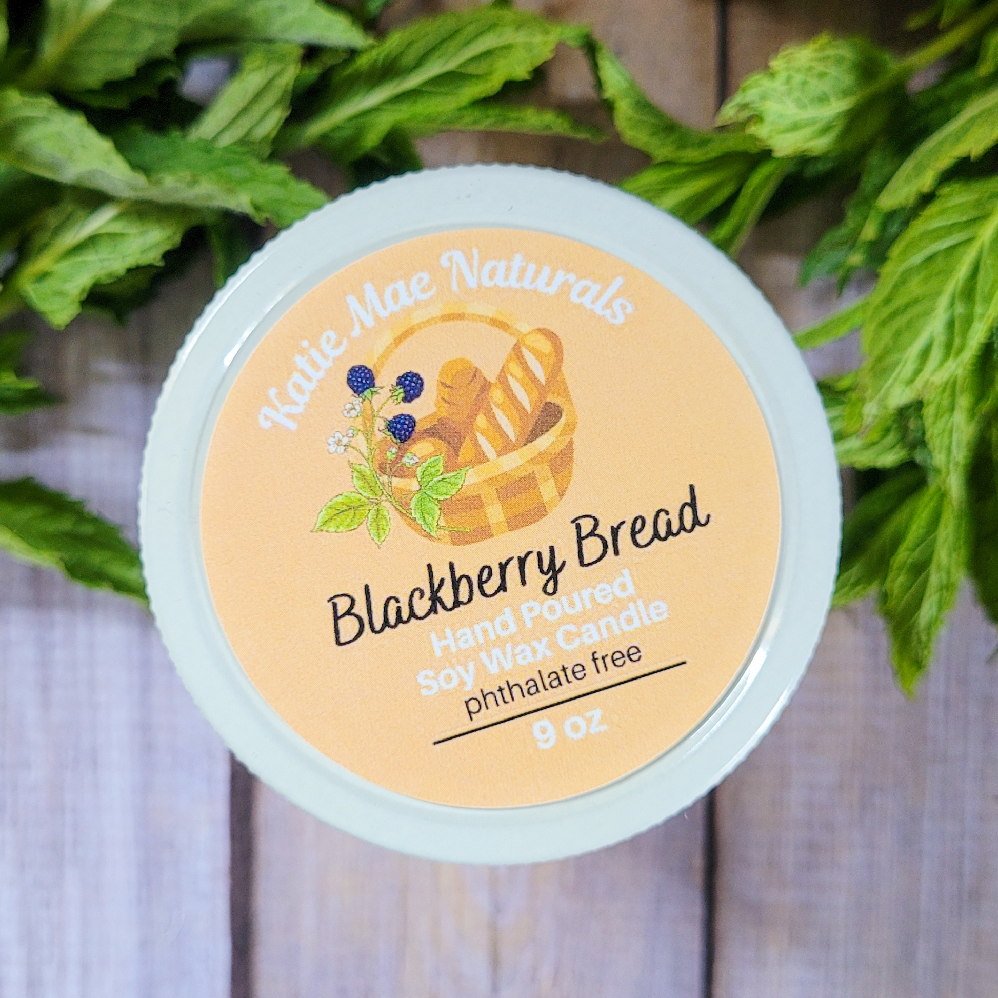 Hand poured soy wax candle labeled 'Blackberry Bread' by Kettle Mae Naturals on a wooden background with greenery.