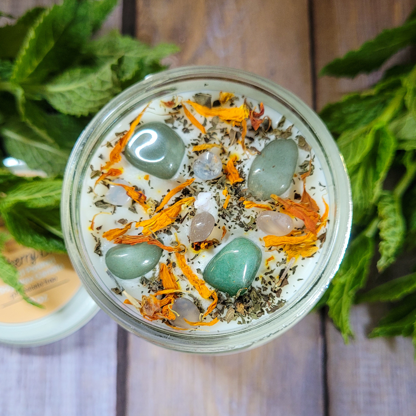 Jar with decorative stones and herbs on a wooden surface with green leaves.