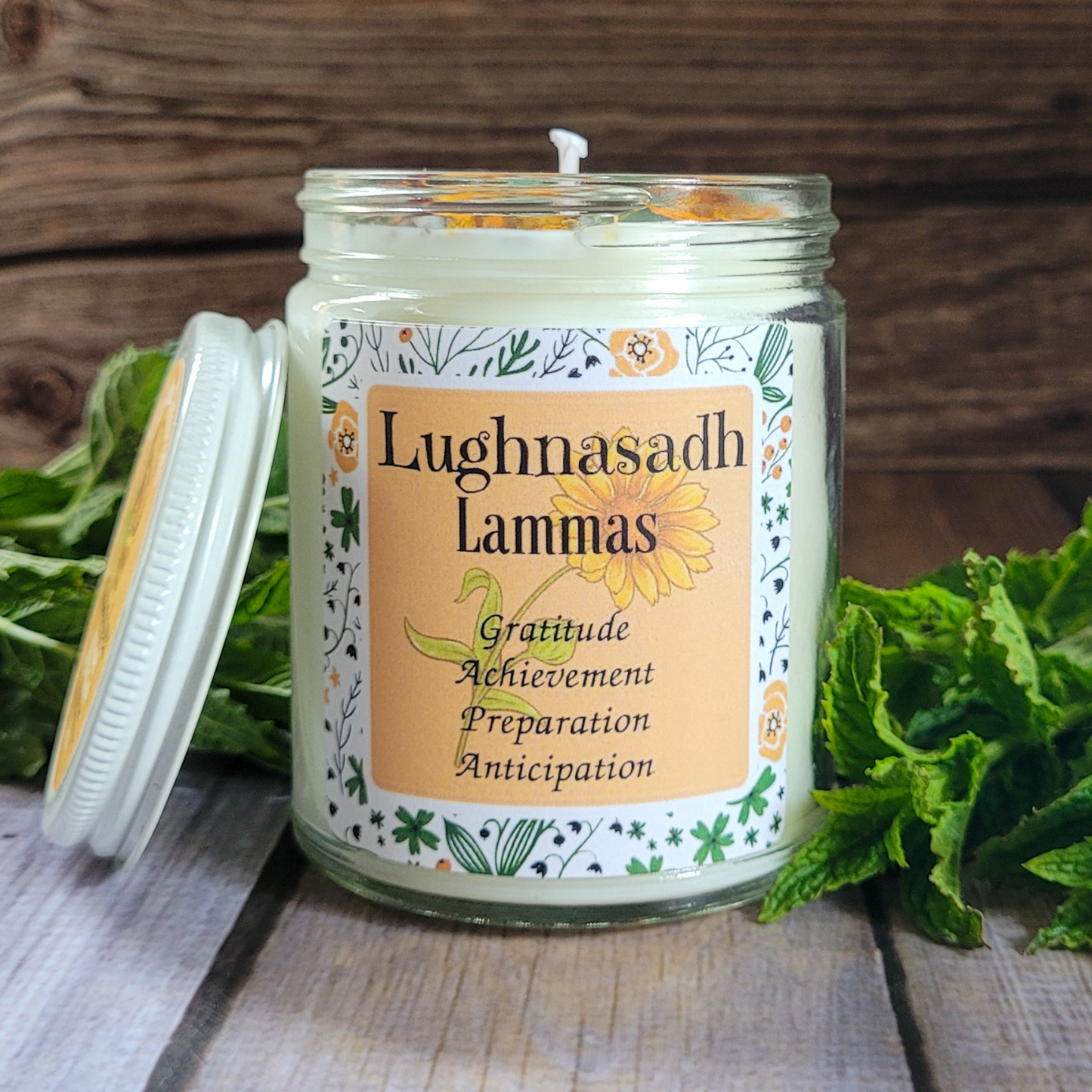 Candle in a glass jar with a decorative label on a wooden surface with greenery.