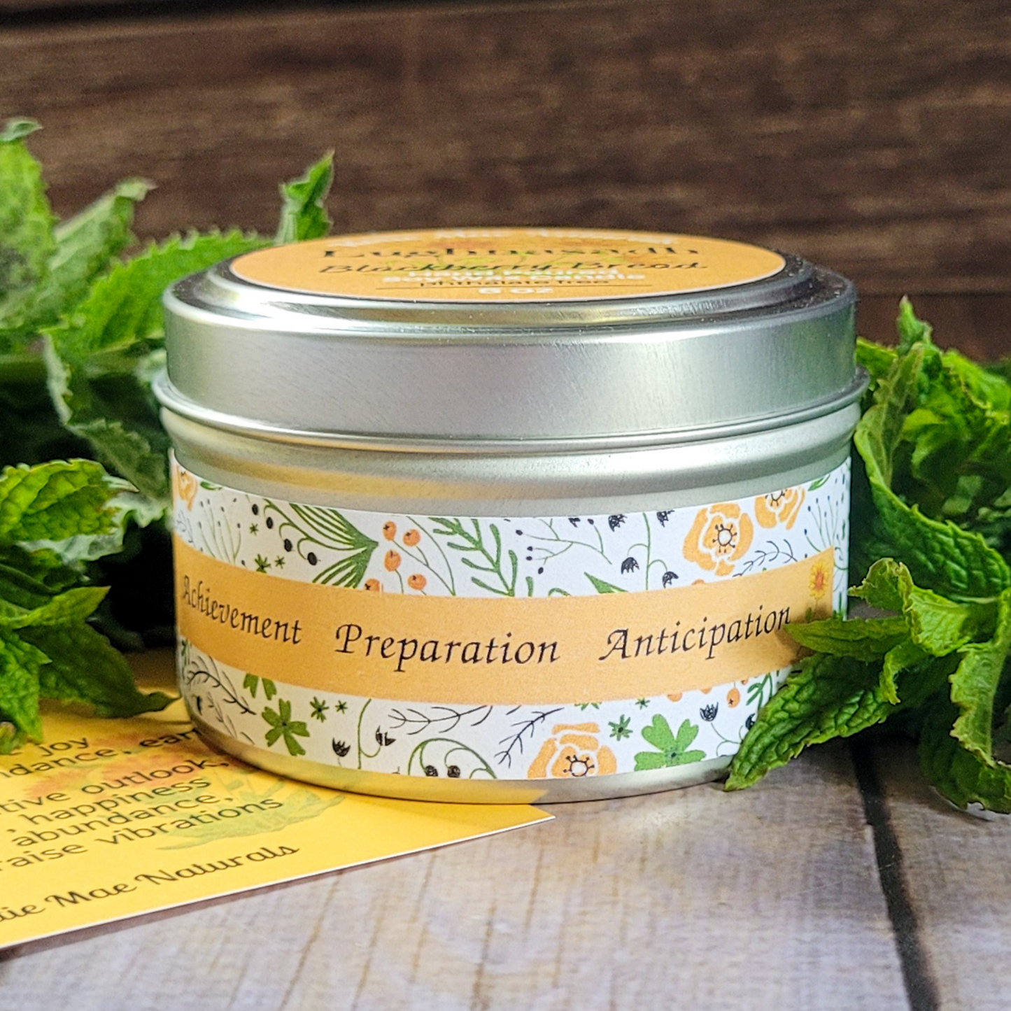 Candle tin with decorative label and green leaves on a wooden surface