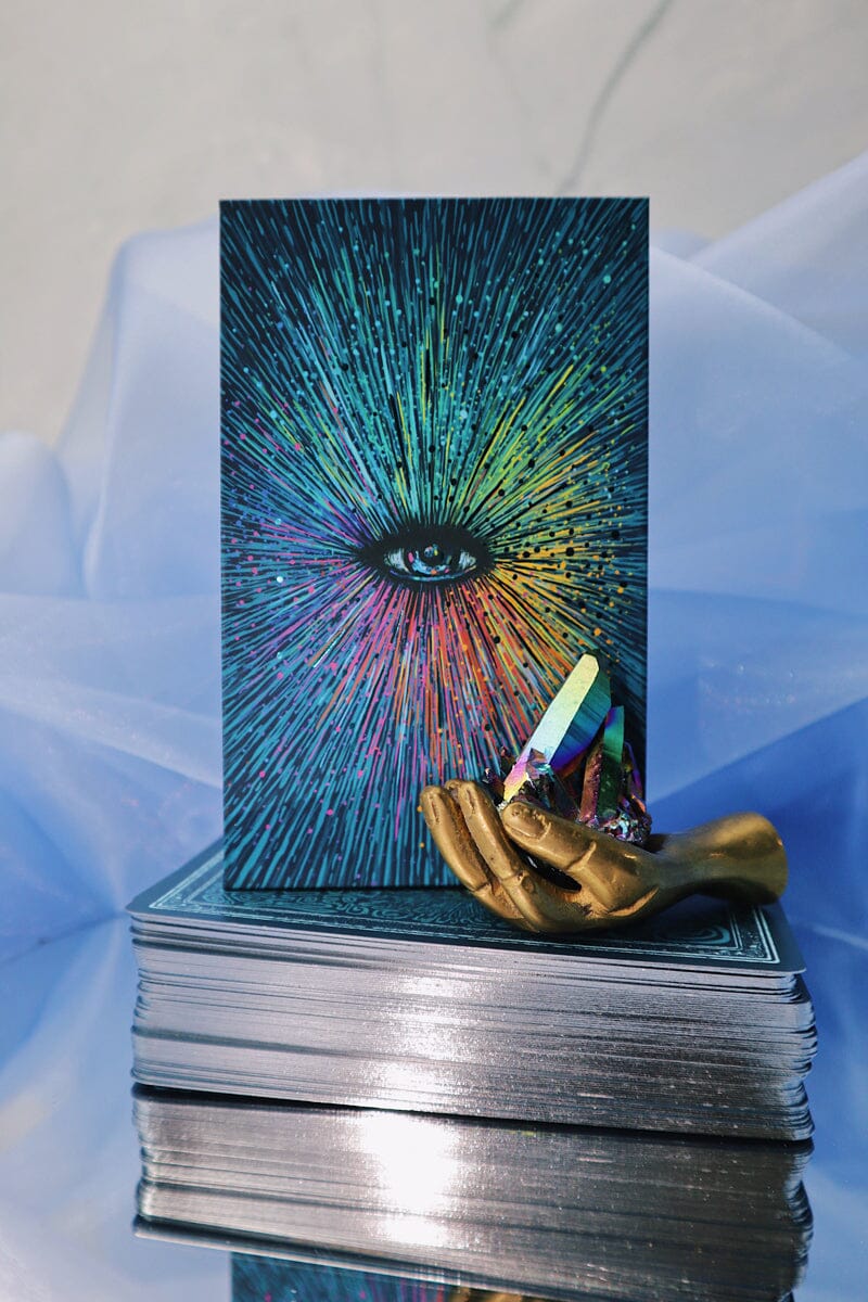 Stack of tarot cards with a colorful design and a gold card holder on a reflective surface.