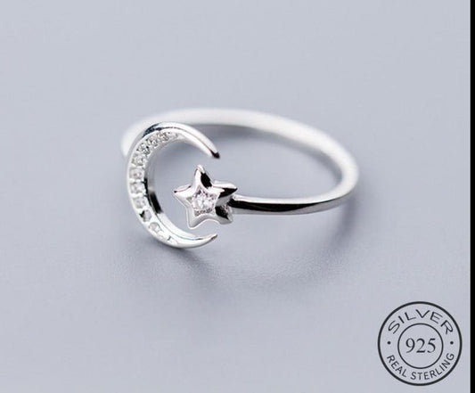 Silver ring with moon and star design on a light gray background