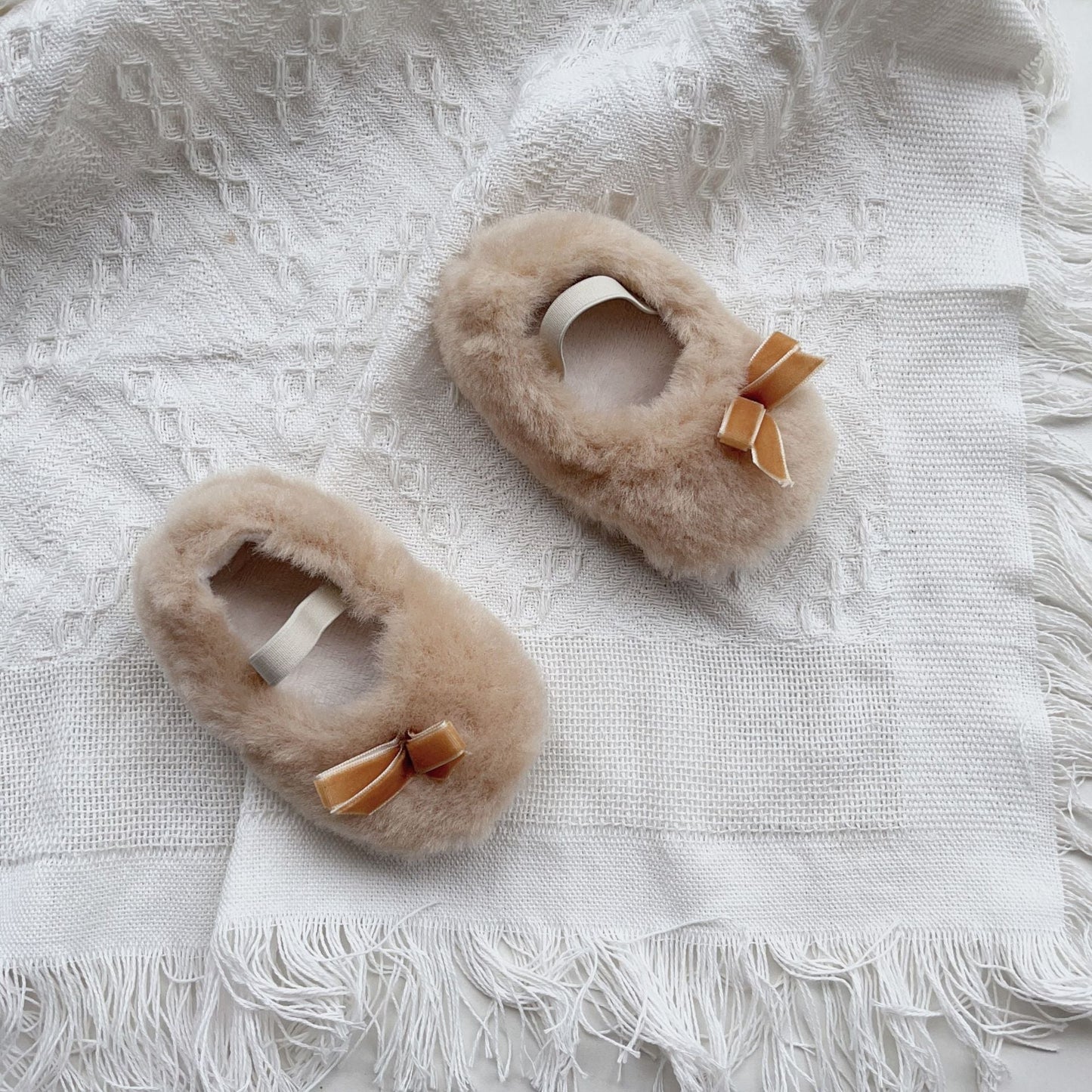 Pair of fluffy slippers with bows on a textured white surface