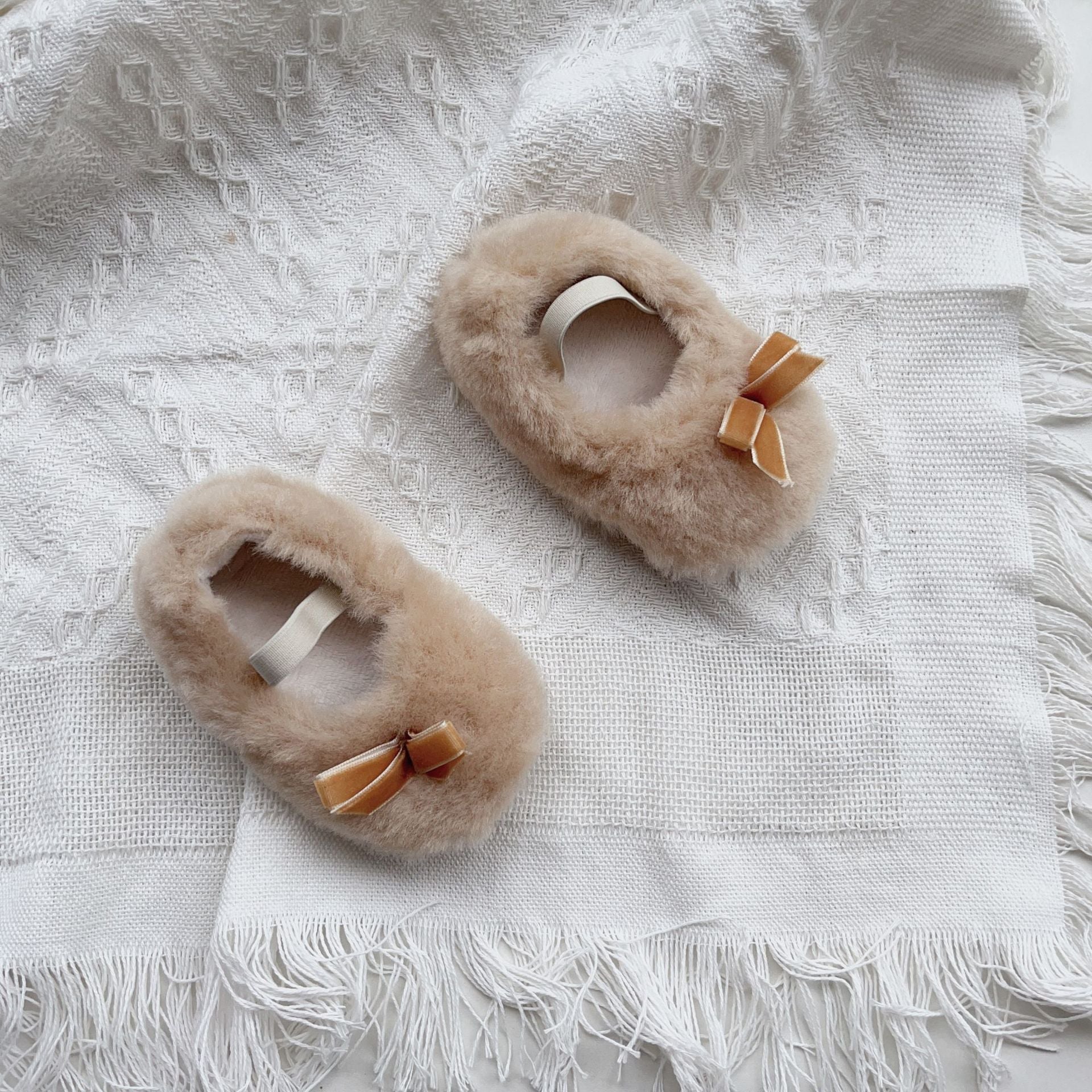 Pair of fluffy slippers with bows on a textured white surface
