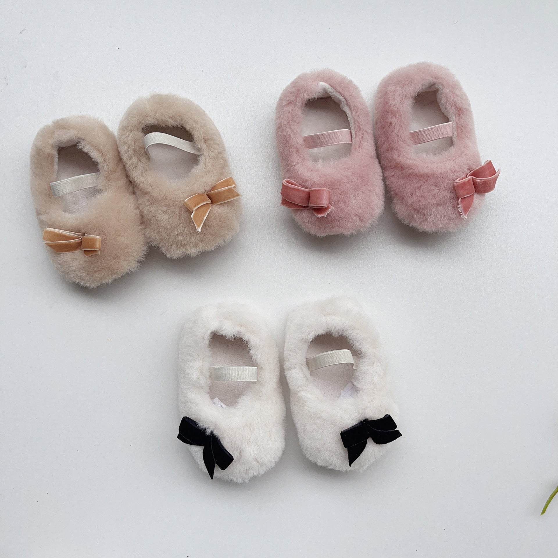 Set of three pairs of fluffy slippers with decorative bows on a white background