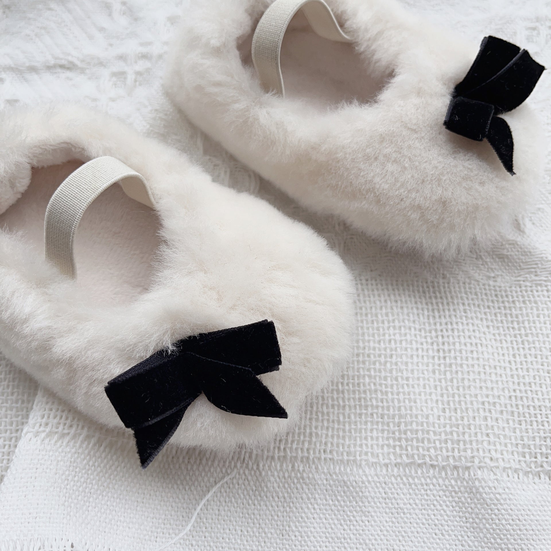 White fluffy slippers with black bows on a textured white surface