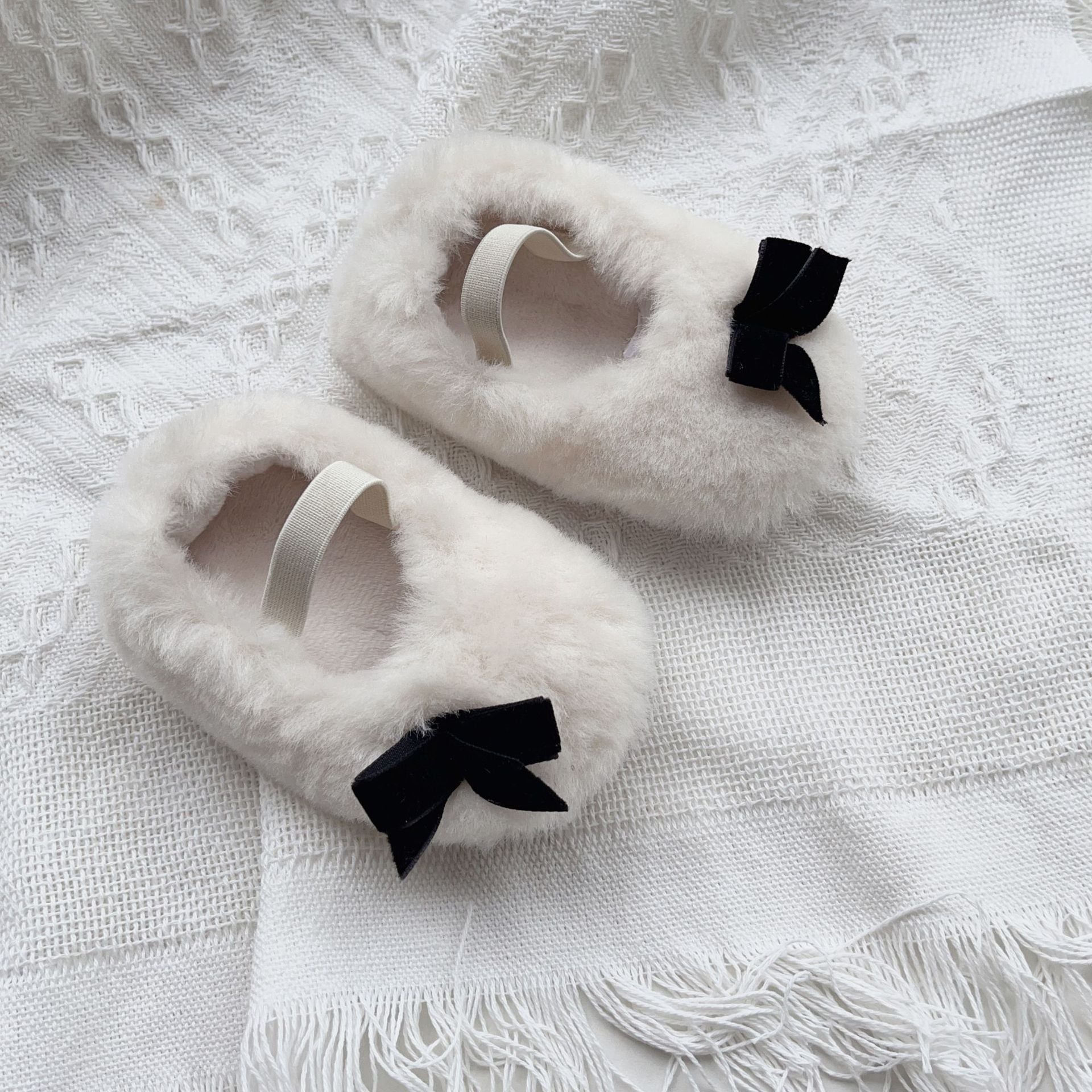 White fluffy slippers with black bows on a textured white surface