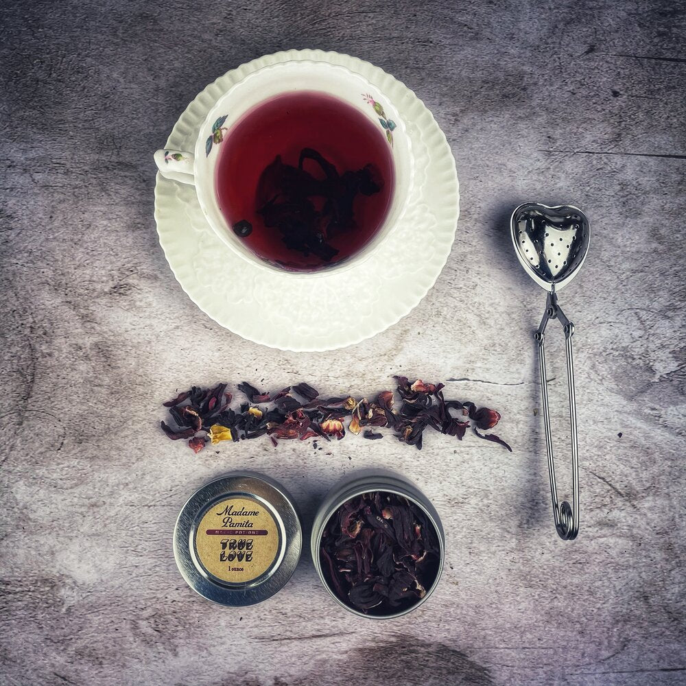 Tea cup with saucer, loose tea leaves, tins of tea, and a tea spoon on a textured surface.
