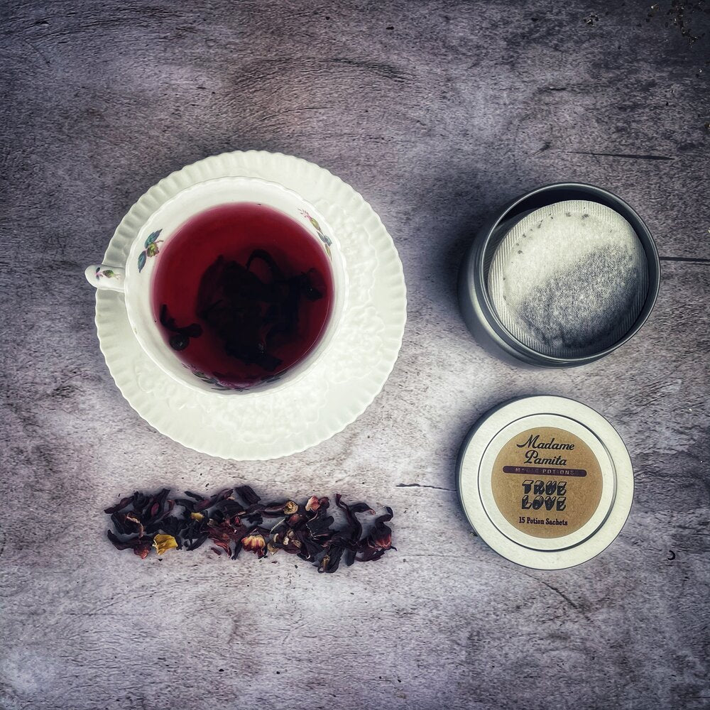 Tea cup with black tea leaves, a small container of cream, and a decorative item on a textured surface.