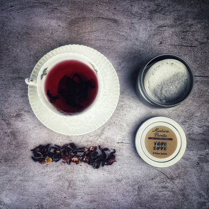 Tea cup with black tea leaves, a small container of cream, and a decorative item on a textured surface.
