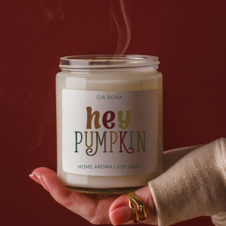 Candle labeled 'hey PUMPKIN' held by a hand against a red background