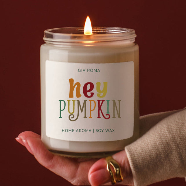 Candle labeled 'hey PUMPKIN' held by a hand with a dark background