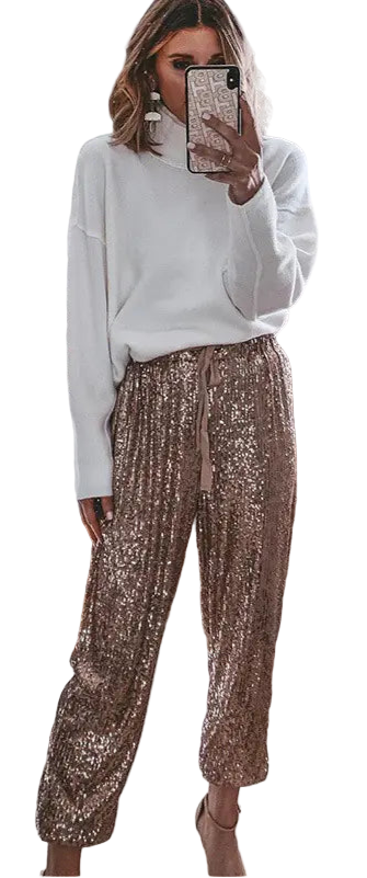 Woman taking a mirror selfie wearing a white sweater and gold sequin pants in a bedroom.