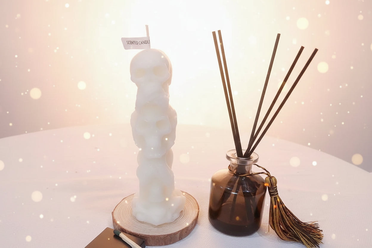 Skull-shaped candle on a wooden base next to a diffuser with black reeds on a white surface.