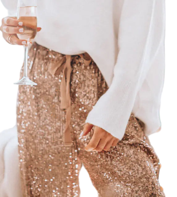 Person wearing gold sequin pants and holding a glass in a festive indoor setting