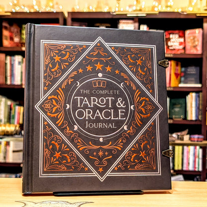 Decorative book titled 'The Complete Tarot & Oracle Journal' on a wooden surface with a bookshelf background.
