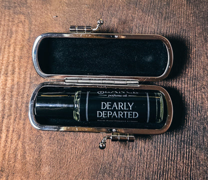 Open case with a perfume bottle labeled 'Dearly Departed' on a wooden surface