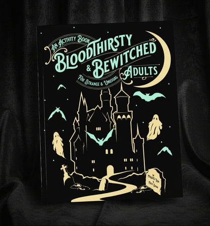 An activity book titled 'Bloodthirsty & Bewitched Adults' with a black cover, teal and gold illustration of a haunted house, bats, ghosts, and a crescent moon, styled on a mint background with ribbon and patterned paper props.